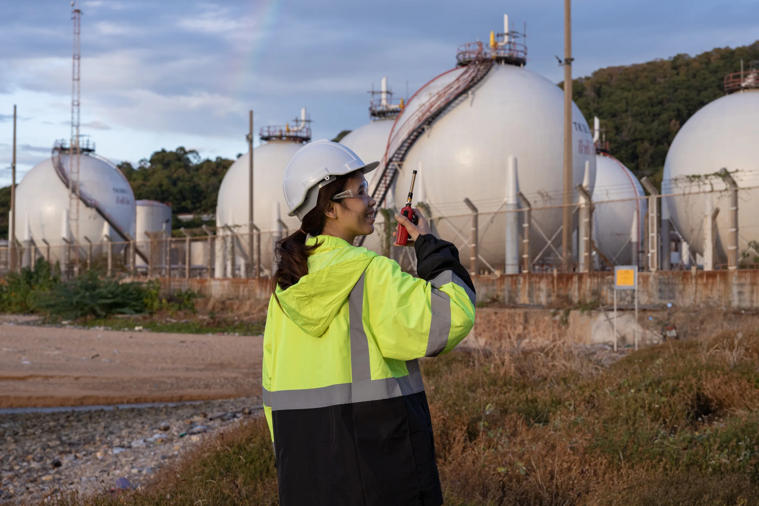 Ingeniera con casco y chaleco de alta visibilidad frente a tanques esféricos de almacenamiento de gas natural