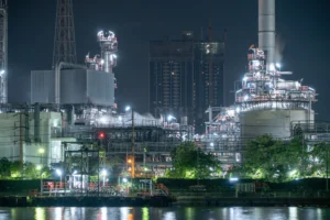 Refinería petroquímica iluminada de noche junto a un río, industria ligada al gas natural y la energía