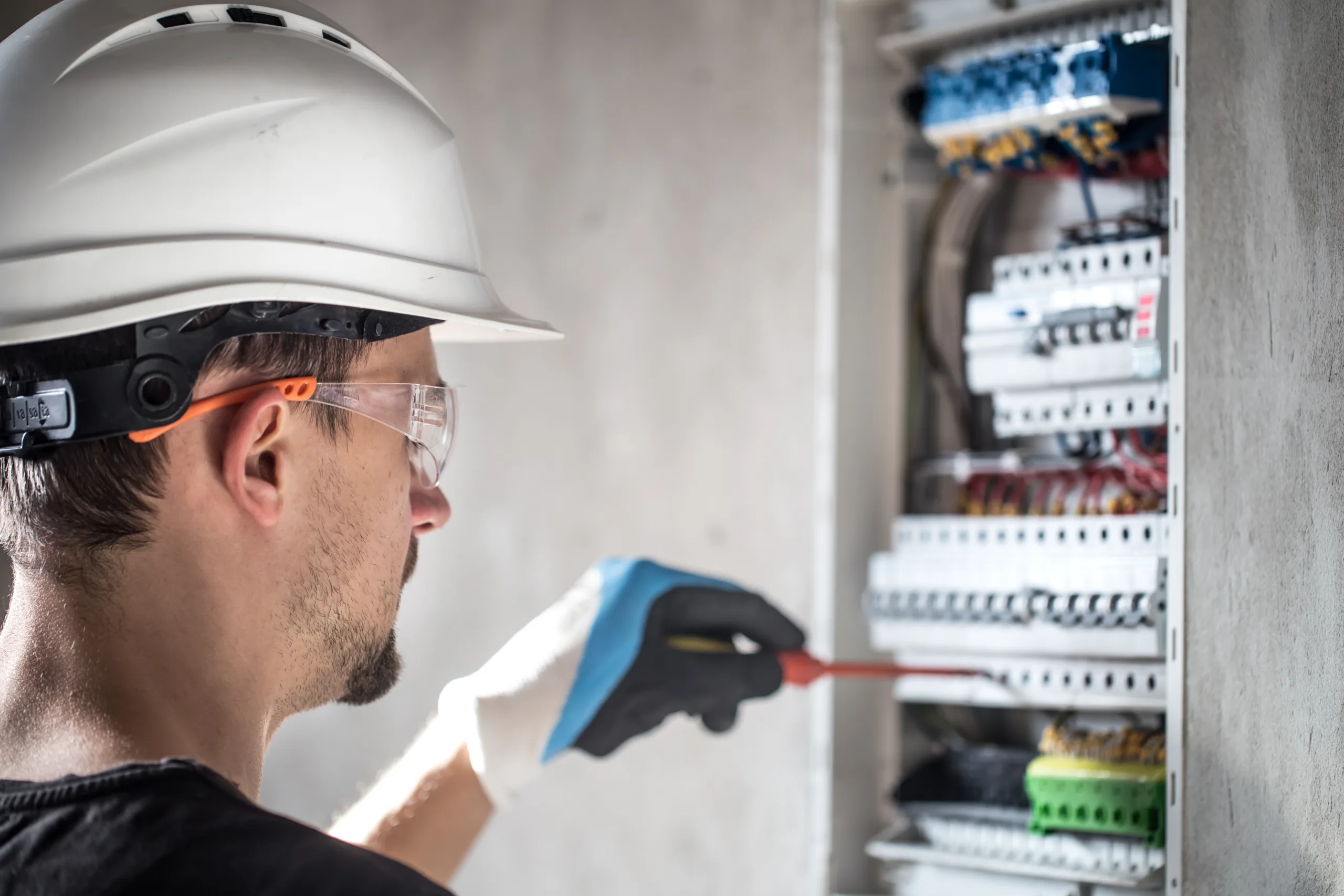Técnico electricista con casco y lentes de seguridad revisando un tablero de distribución eléctrica
