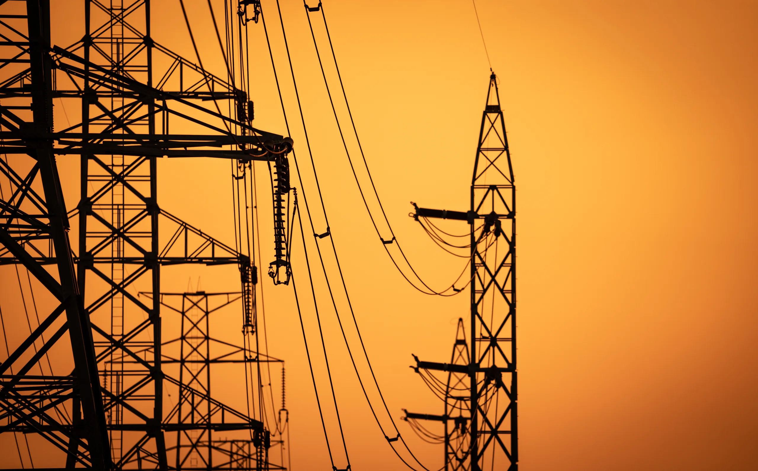 Silueta de torres de transmisión de alta tensión y cables eléctricos contra un atardecer naranja